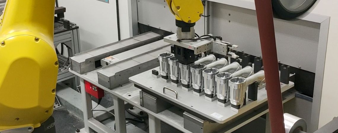 Il braccio robotico FANUC M-20iB collabora con sistemi di alimentazione a tavolo scorrevole per l'automazione della lucidatura